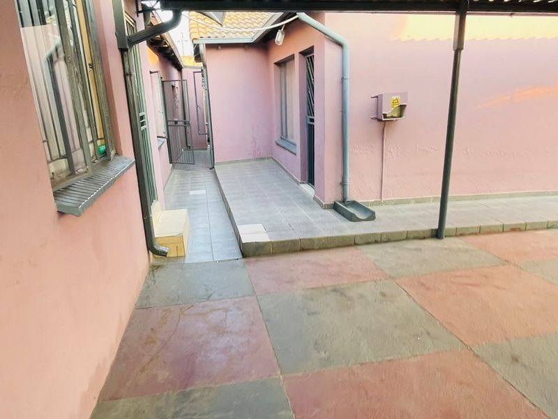 A paved rear courtyard area featuring a covered patio section, security gates, and external building infrastructure.