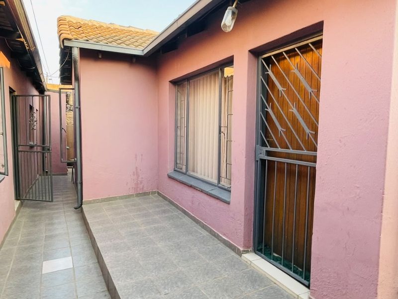 A side exterior view of the property featuring a tiled patio area, security gates, and pink exterior walls.