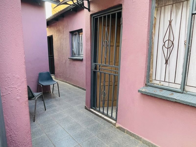 A narrow outdoor patio area featuring tiled flooring, a security gate, and protective window bars, providing a functional transition space.