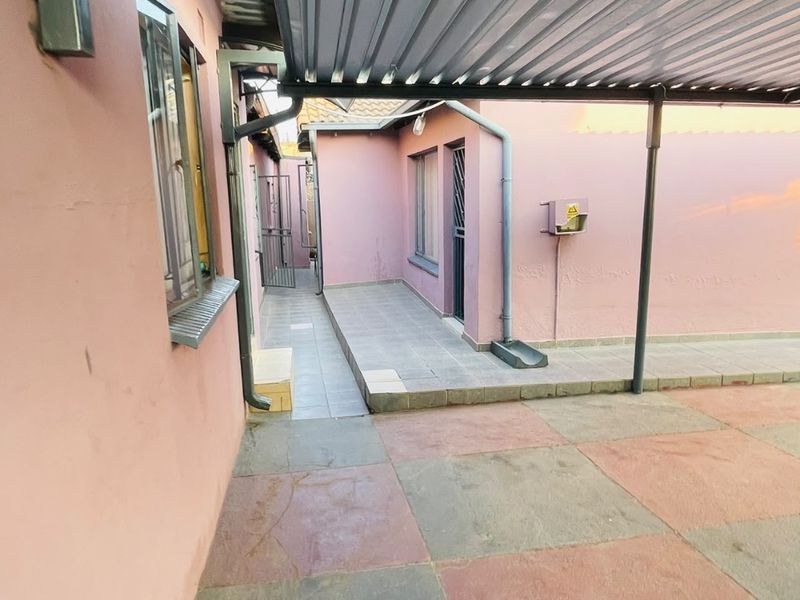 A rear exterior view showing a covered patio area with tiled flooring, metal roofing, and access to the side of the house.