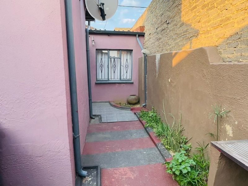 A narrow rear exterior passage featuring a paved walkway, boundary wall, and exterior building access with a satellite dish installation.