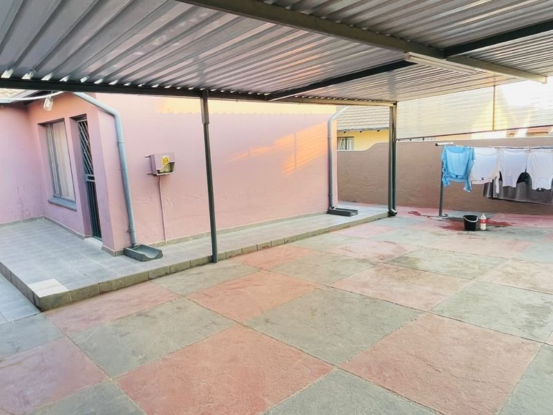 A covered outdoor patio area featuring a corrugated metal roof, metal support posts, and tiled flooring, providing a functional space for outdoor activities.