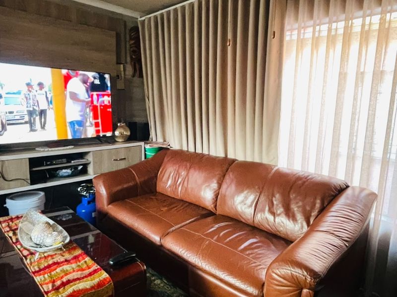 A cozy living room featuring a built-in media unit, recessed ceiling lighting, and floor-to-ceiling curtains providing natural light control.