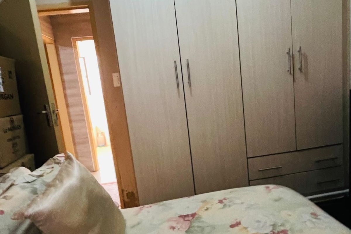 A bedroom featuring a built-in wardrobe with light wood-finish cabinetry and a view into an adjacent hallway.