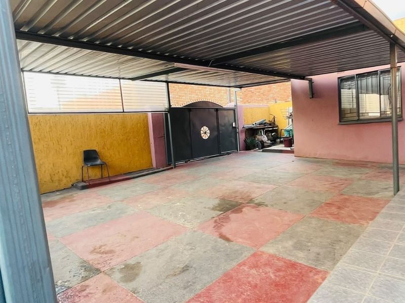 A covered outdoor parking area or garage featuring a corrugated metal roof, tiled flooring, and a secure metal gate.