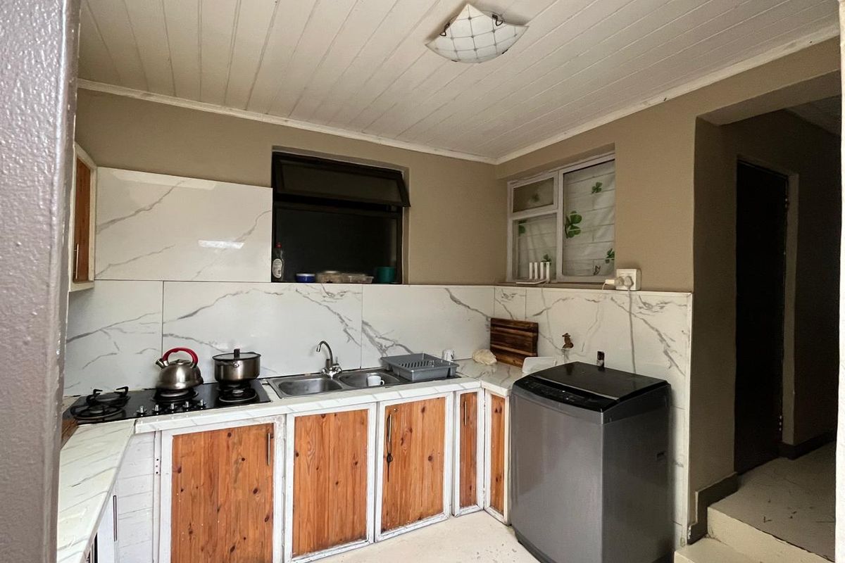 Functional kitchen featuring marble-look splashbacks, built-in wooden cabinetry, a gas hob, and a double sink, with direct access to an adjacent hallway.