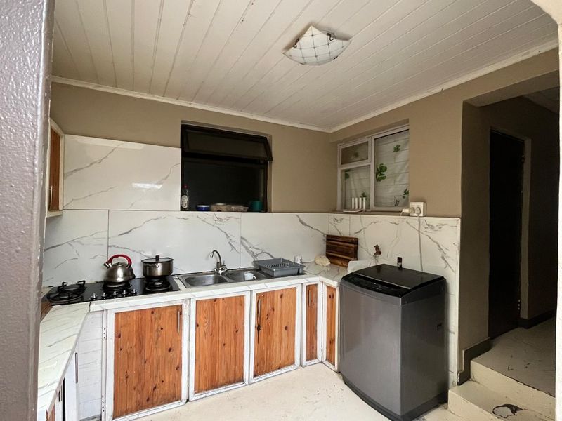Functional kitchen featuring marble-look splashbacks, built-in wooden cabinetry, a gas hob, and a double sink, with direct access to an adjacent hallway.