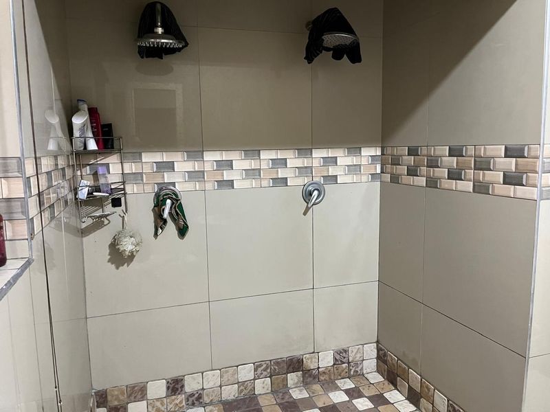 A walk-in shower enclosure featuring dual shower heads, neutral wall tiling, and a decorative mosaic tile border with a matching mosaic tiled floor.