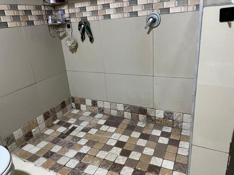A shower enclosure featuring a linear drain, tiled flooring, and wall tiling with a shower mixer fixture.