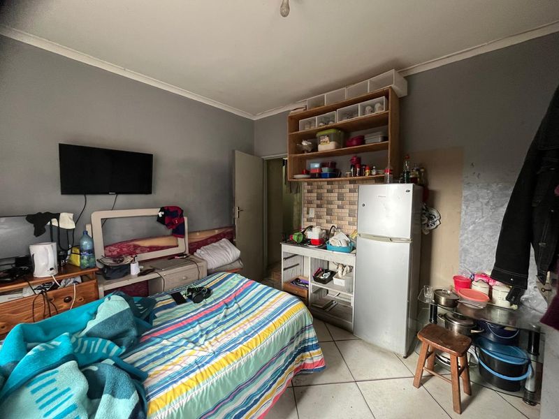 A multi-functional bedroom space featuring tiled flooring and built-in shelving, currently utilized as a combined living and kitchenette area.