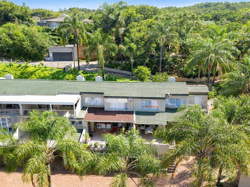 Aerial view of a multi-level apartment complex featuring tiled roofing, covered patio areas, and lush surrounding greenery.