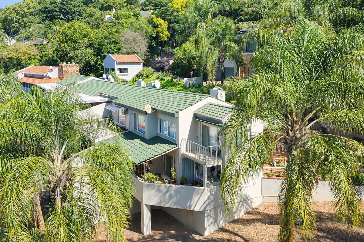 Aerial view of a multi-level apartment building featuring a green tiled roof, balconies, and surrounding lush garden landscaping.