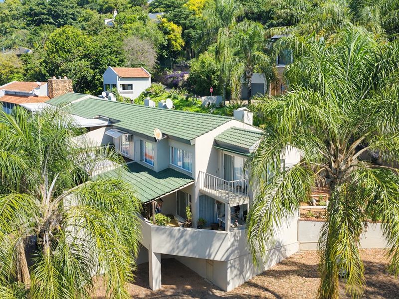 Aerial view of a multi-level apartment building featuring a green tiled roof, balconies, and surrounding lush garden landscaping.