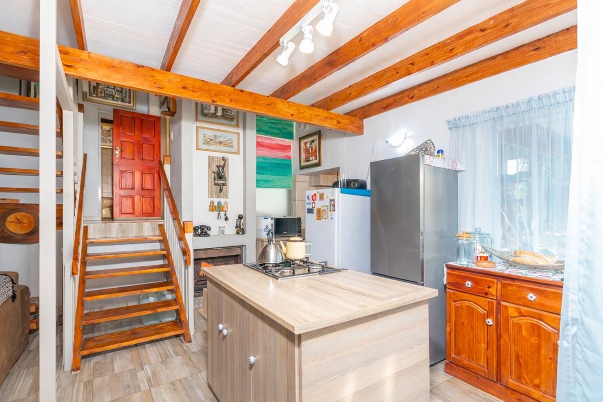 A rustic kitchen area featuring exposed timber ceiling beams, a central island with a built-in hob, and a wooden staircase leading to an upper level.