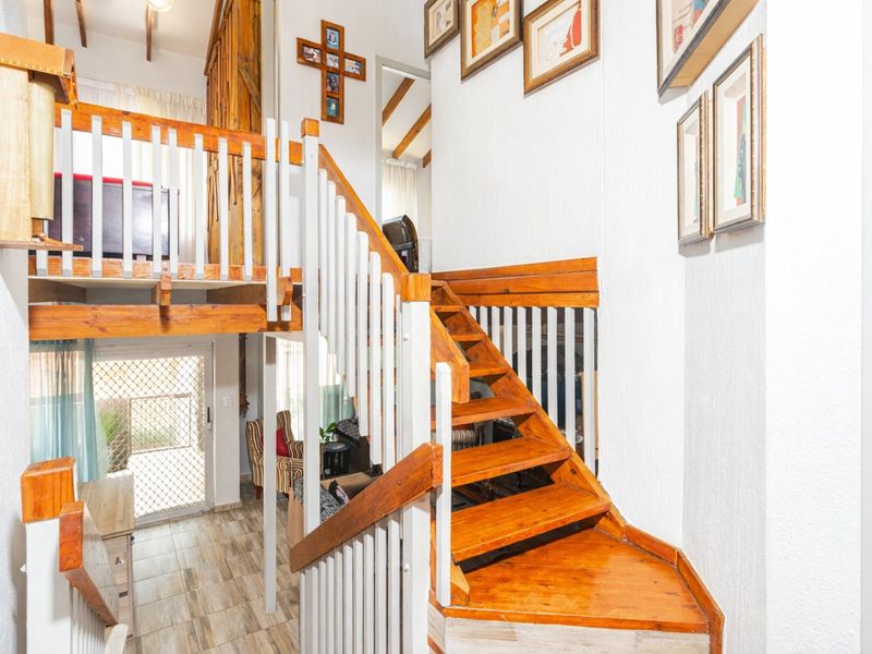 A multi-level hallway featuring a wooden staircase, mezzanine landing, tiled flooring, and exposed timber ceiling beams, providing access to the lower living area.