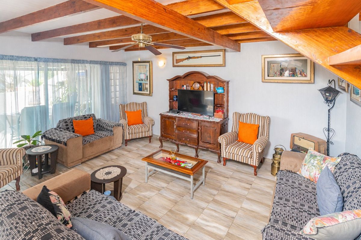 A living room featuring exposed timber ceiling beams, tiled flooring, and an integrated staircase, offering a rustic aesthetic with potential for modern updates.