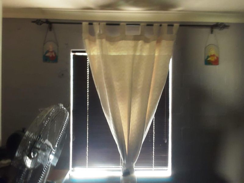 A bedroom interior featuring a window with installed blinds and a curtain rod, showing signs of wear on the surrounding wall surfaces.