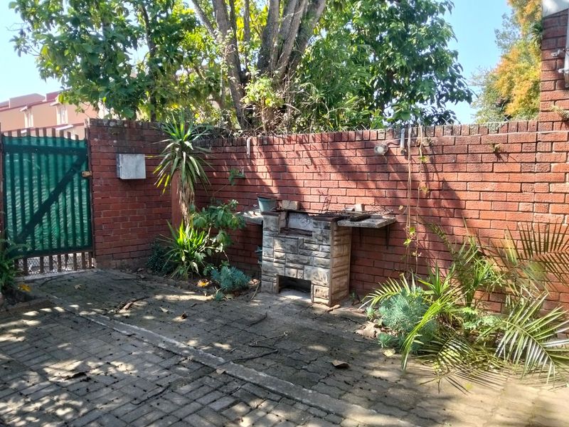 A private rear courtyard featuring a built-in brick braai, paved flooring, and a secure pedestrian gate, offering potential for an outdoor entertainment area.