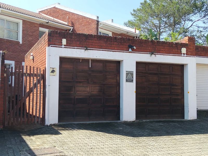 A double garage with timber doors and brick exterior, featuring paved driveway access and integrated security lighting.