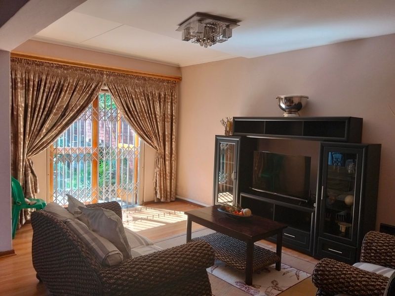 A comfortable living room featuring laminate flooring and a sliding glass door with security gate, providing access to the outdoor area.