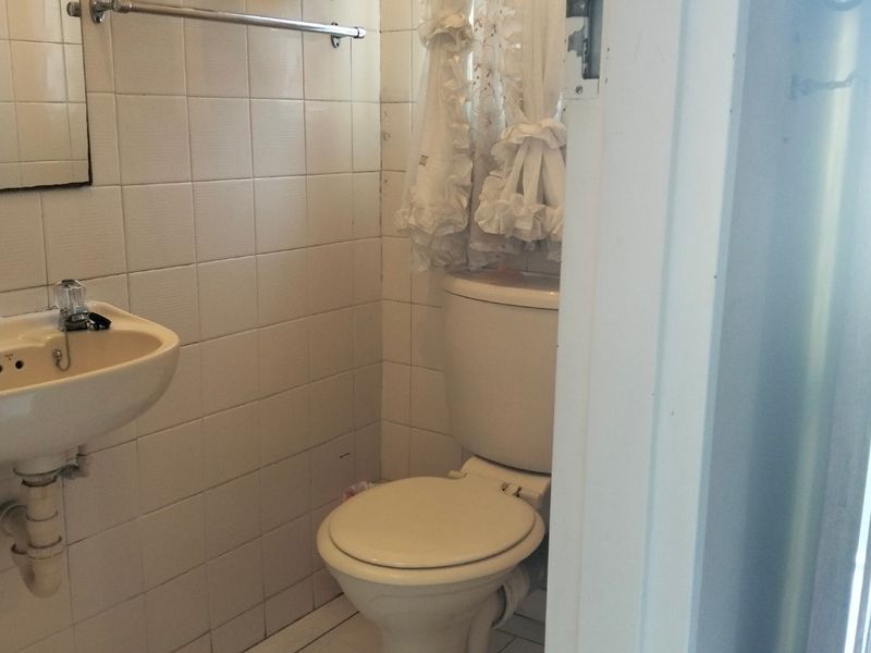 A compact bathroom featuring a wall-mounted basin, toilet, and tiled finishes, requiring modernization to improve its overall aesthetic and functionality.