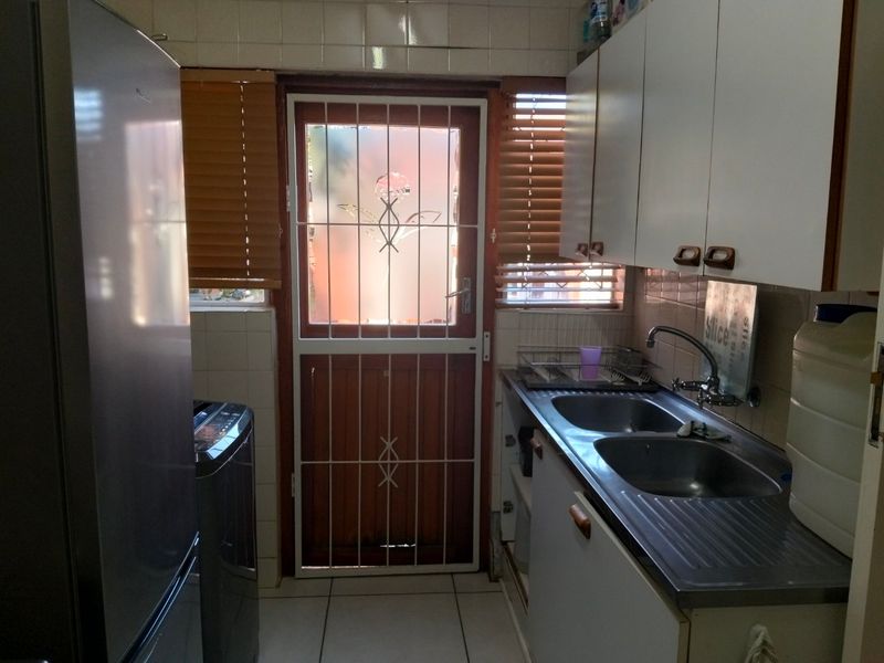 A functional kitchen featuring double stainless steel sinks, tiled splashbacks, and built-in cabinetry with direct access to the exterior via a security gate.
