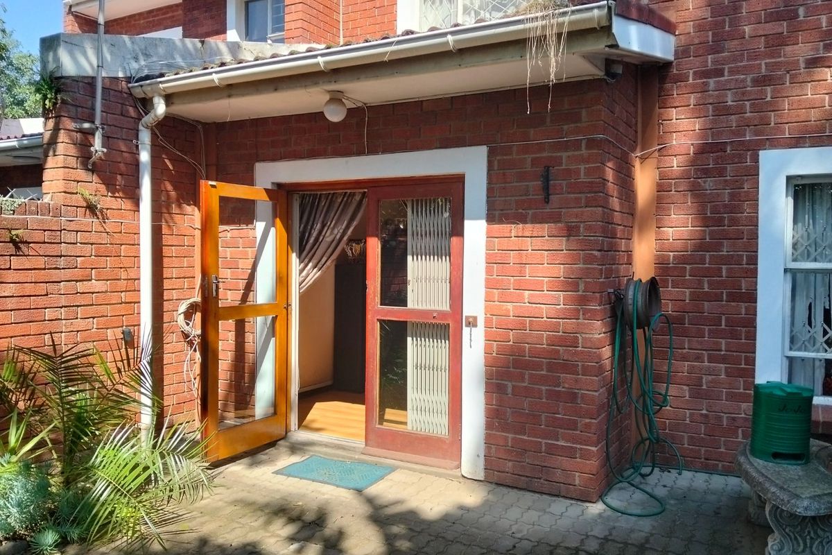 Rear exterior view of the townhouse featuring a brick facade, paved patio area, and timber-framed glass door access.