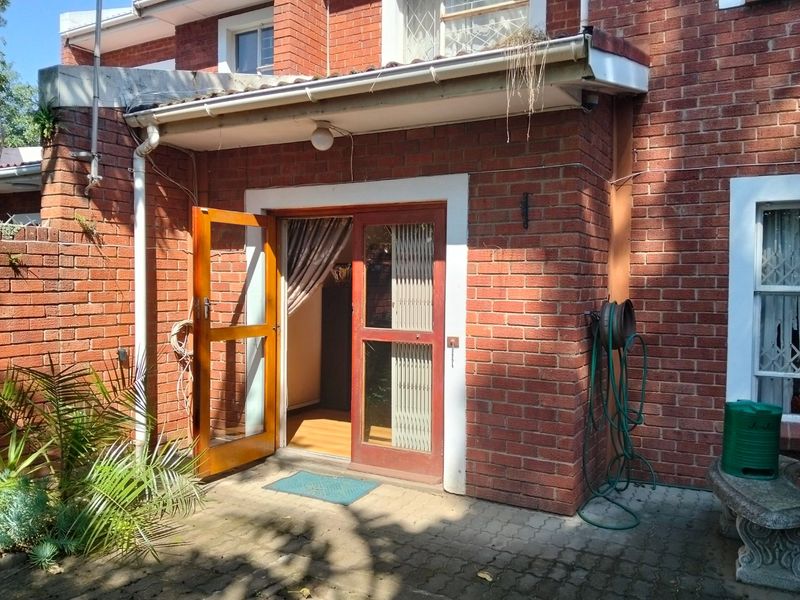 Rear exterior view of the townhouse featuring a brick facade, paved patio area, and timber-framed glass door access.
