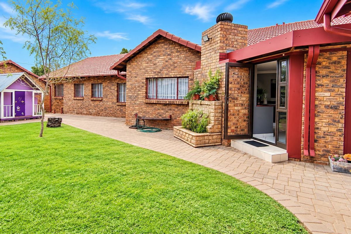 A well-maintained rear exterior view featuring a brick facade, tiled roof, paved patio area, and a spacious lawn.