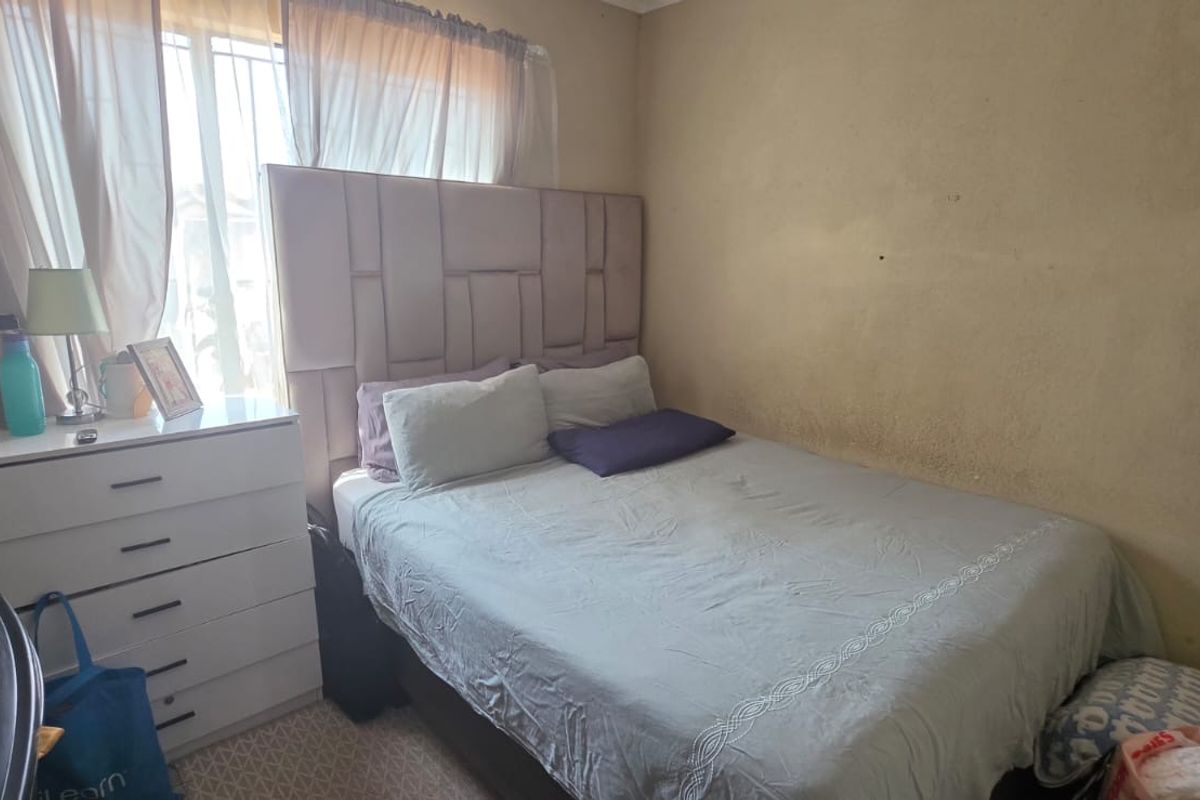 A compact bedroom featuring carpeted flooring and a window fitted with security bars, requiring cosmetic updates to the wall finishes.