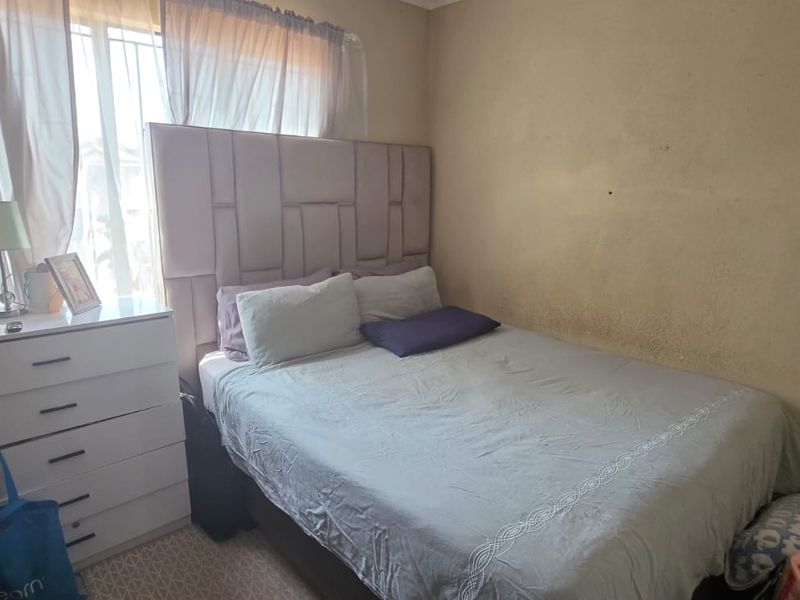 A compact bedroom featuring carpeted flooring and a window fitted with security bars, requiring cosmetic updates to the wall finishes.