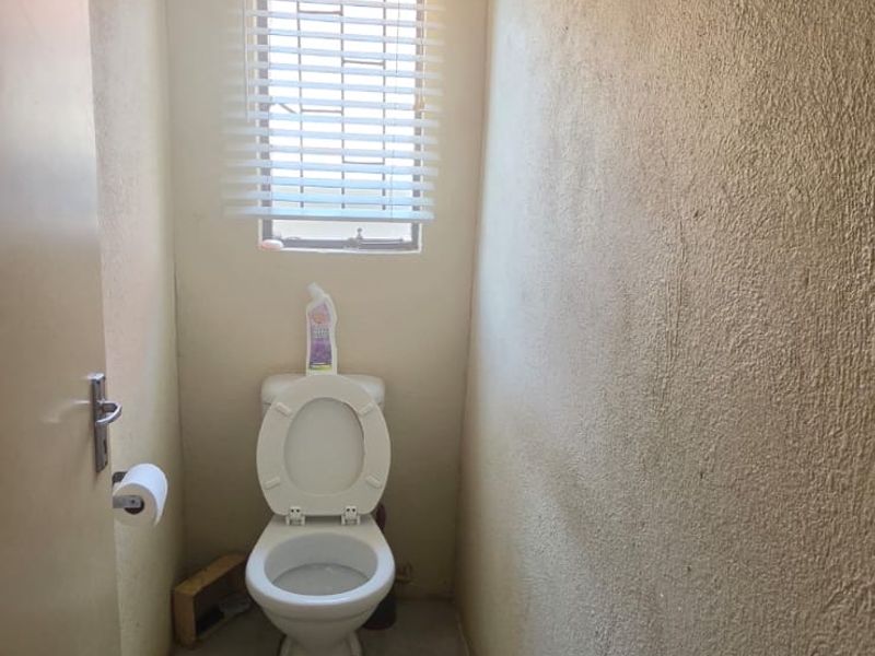 A compact guest toilet featuring tiled flooring, a window with fitted blinds, and a standard toilet fixture.