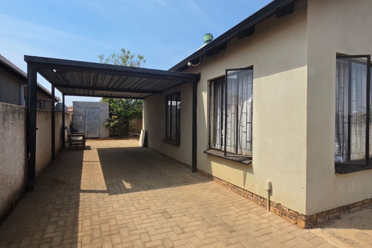 Rear exterior view of the property featuring a paved driveway, a covered carport, and security bars on the windows.