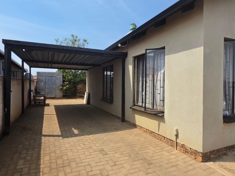 Rear exterior view of the property featuring a paved driveway, a covered carport, and security bars on the windows.