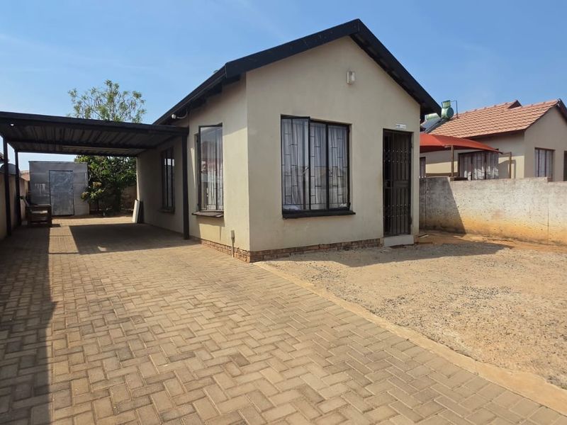 Front view of a detached house featuring a paved driveway, a covered carport, and a perimeter wall with security bars on windows.