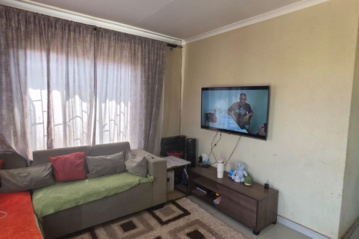 A living room area featuring tiled flooring and curtain rails, currently showing signs of wear on the wall surfaces.