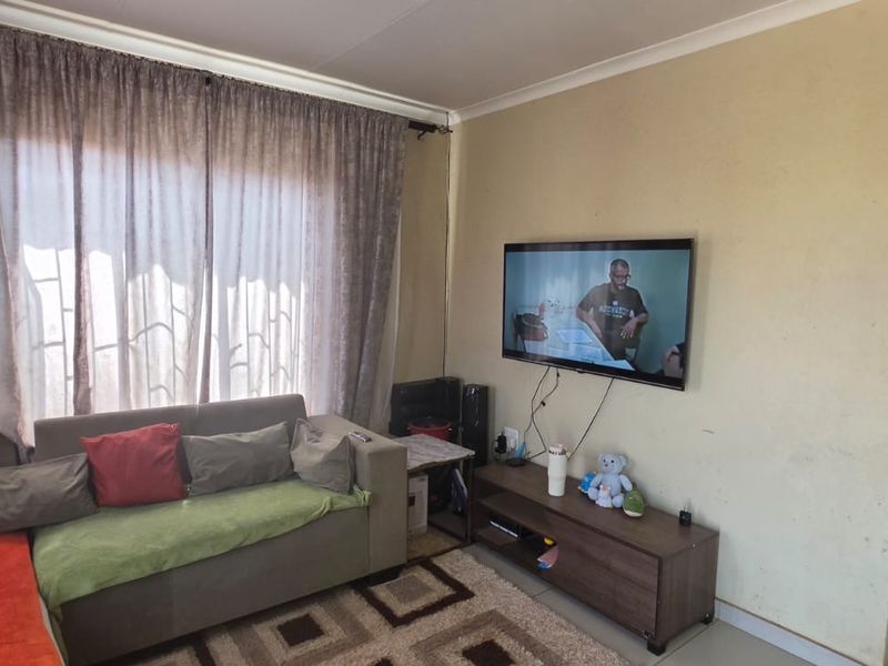 A living room area featuring tiled flooring and curtain rails, currently showing signs of wear on the wall surfaces.
