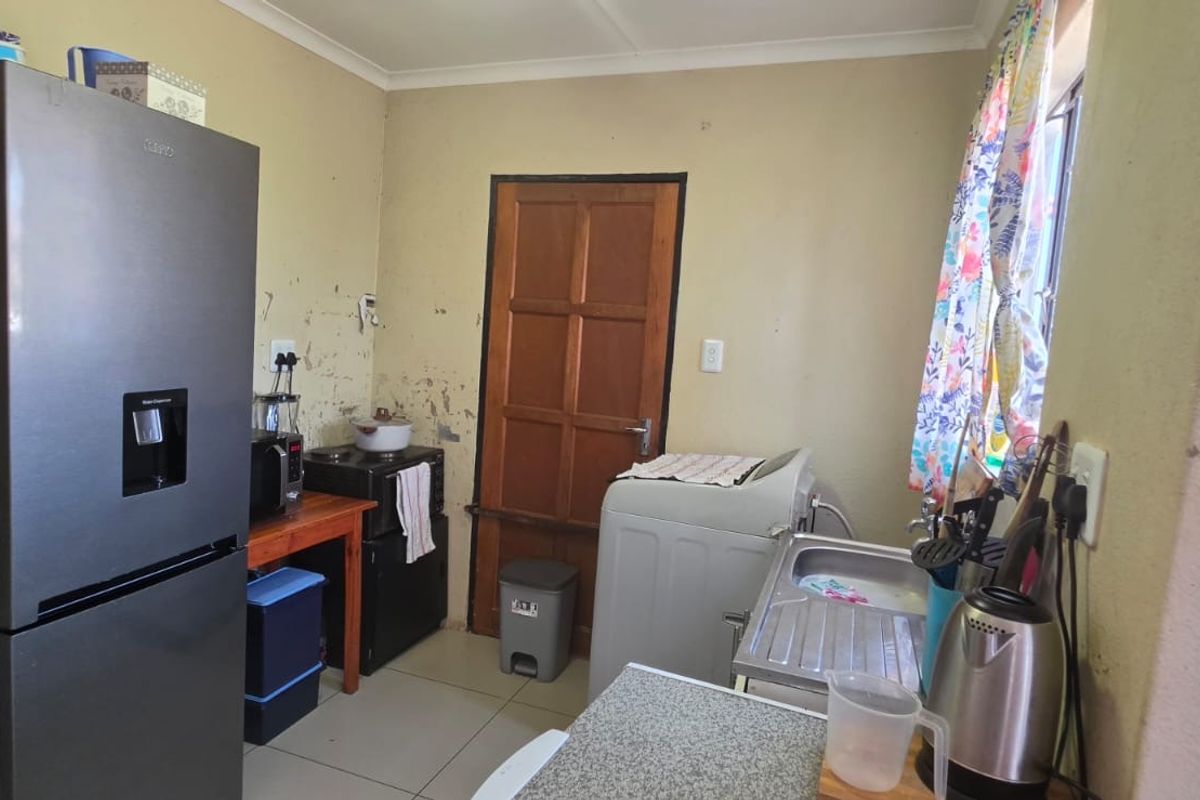 A functional kitchen area featuring tiled flooring, a stainless steel sink, and a timber door, currently requiring cosmetic wall repairs and repainting.
