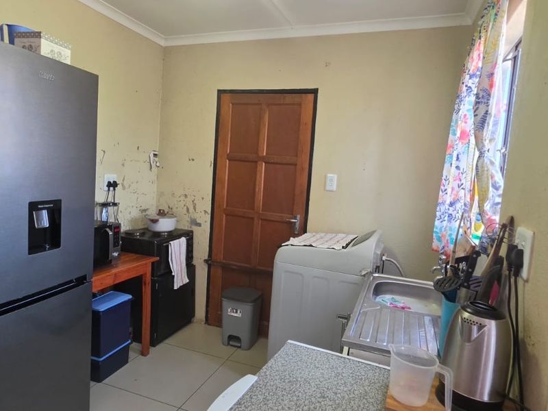 A functional kitchen area featuring tiled flooring, a stainless steel sink, and a timber door, currently requiring cosmetic wall repairs and repainting.