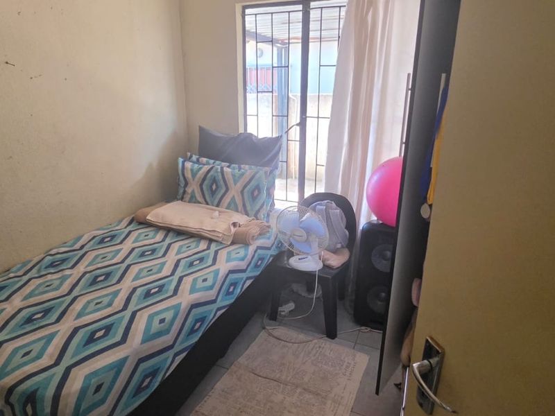 A compact bedroom featuring a window with a security gate and neutral wall finishes, offering a functional space for a single bed.