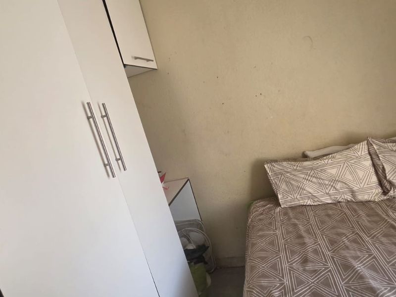 A compact bedroom featuring a built-in wardrobe and overhead storage unit, requiring cosmetic updates to the wall finishes.