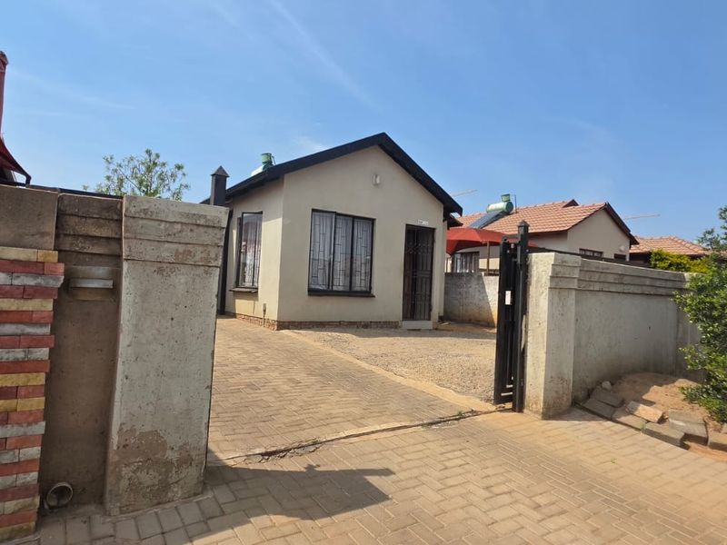 Front view of a detached house featuring a paved driveway, perimeter wall with security gate, and installed solar geyser.