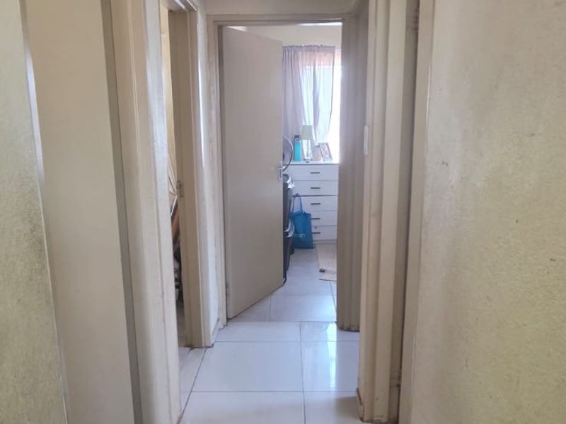 A functional hallway featuring neutral tiled flooring, a ceiling access hatch, and multiple doorways leading to adjacent rooms.