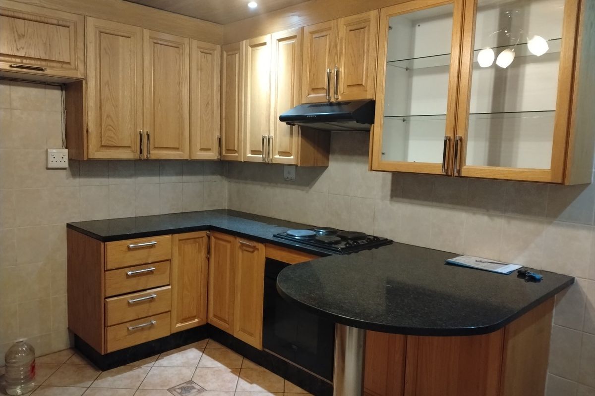 A functional kitchen featuring oak cabinetry, granite countertops, a built-in oven, electric hob, and a breakfast bar with tiled finishes.