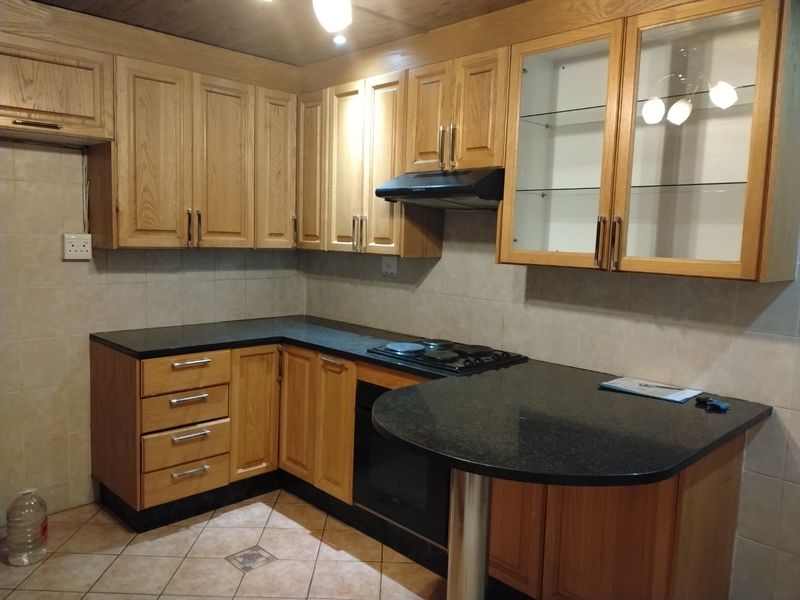 A functional kitchen featuring oak cabinetry, granite countertops, a built-in oven, electric hob, and a breakfast bar with tiled finishes.