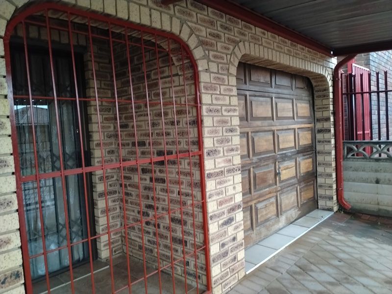 Front exterior view featuring a face brick facade, a wooden garage door, and a metal security gate over the entrance.