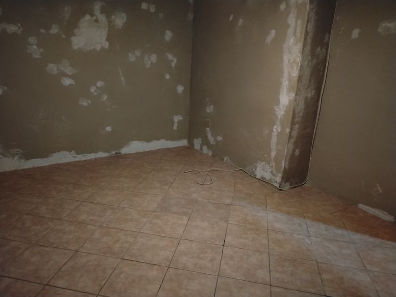 An empty room featuring ceramic floor tiles and walls currently undergoing plastering and surface preparation.