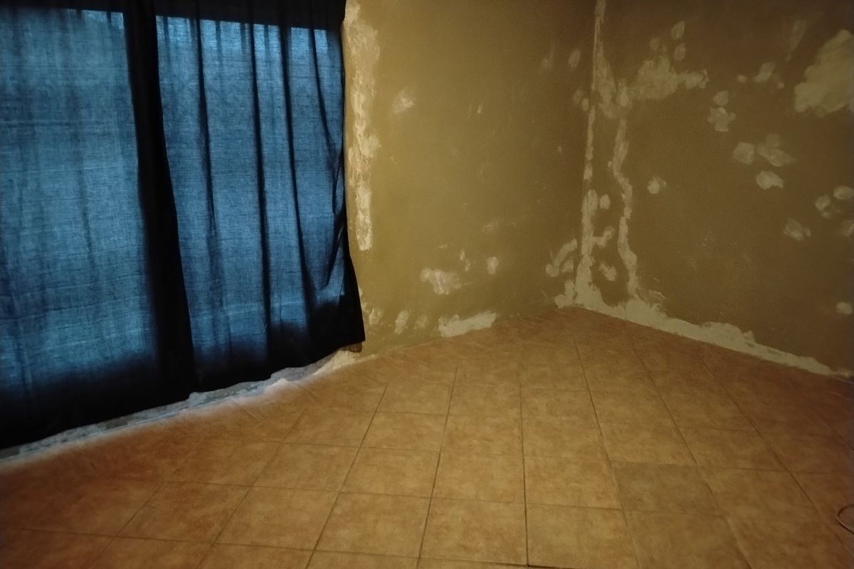 An empty bedroom featuring tiled flooring and walls showing significant plaster damage and signs of moisture.
