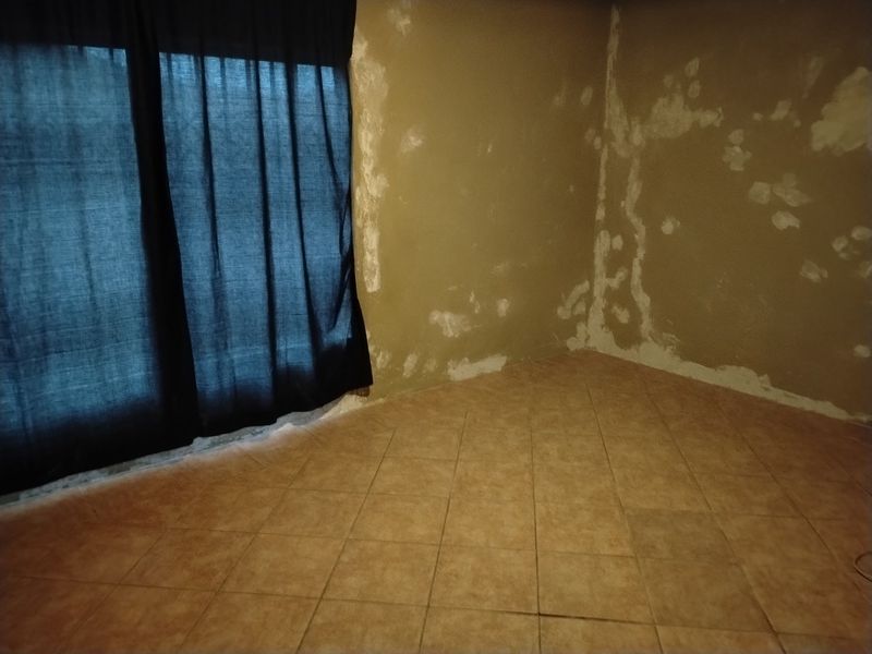 An empty bedroom featuring tiled flooring and walls showing significant plaster damage and signs of moisture.