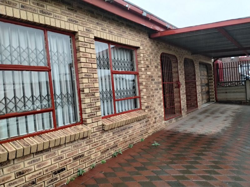 Front exterior view of a face brick house featuring a paved driveway, carport, and secure metal window and door fittings.